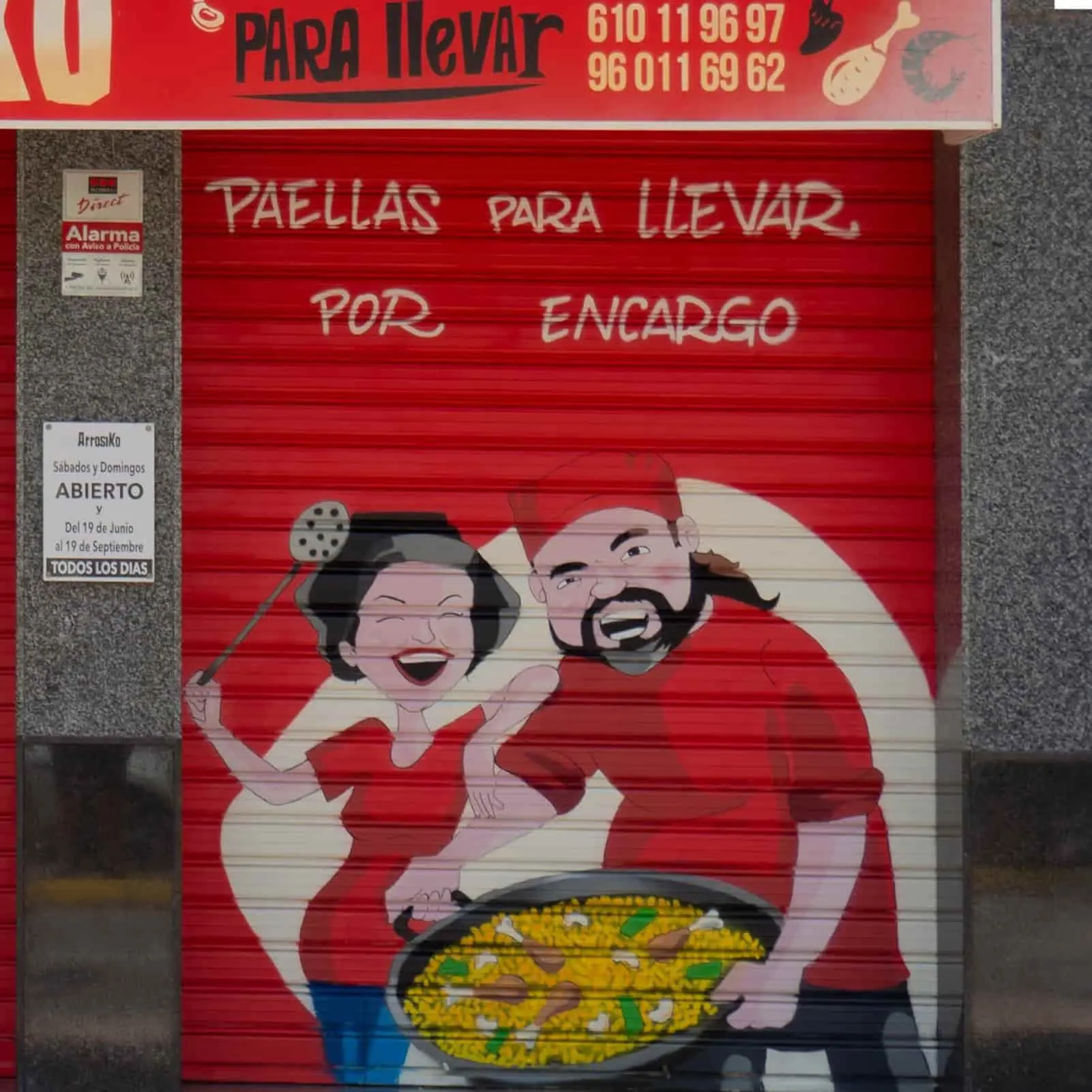 mural exterior sobre persiana de dos personas sosteniendo una paella